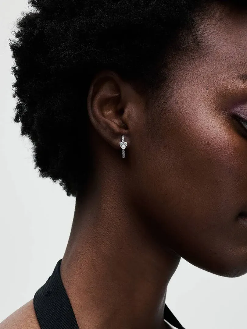 Zijaanzicht close-up van een oorring met hartvormige edelsteen gedragen in het oor, neutrale achtergrond.