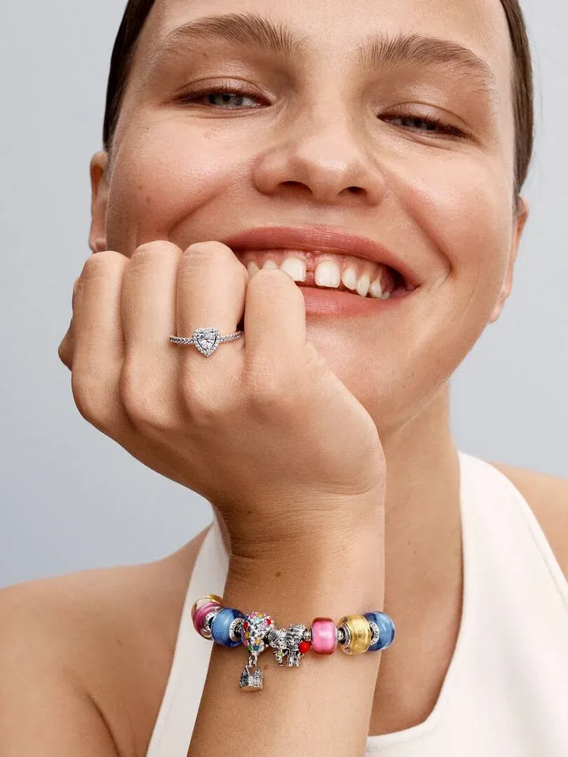 Nahaufnahme einer lächelnden Frau mit dem Charm am Handgelenk und einem Ring am Finger, neutraler Hintergrund.