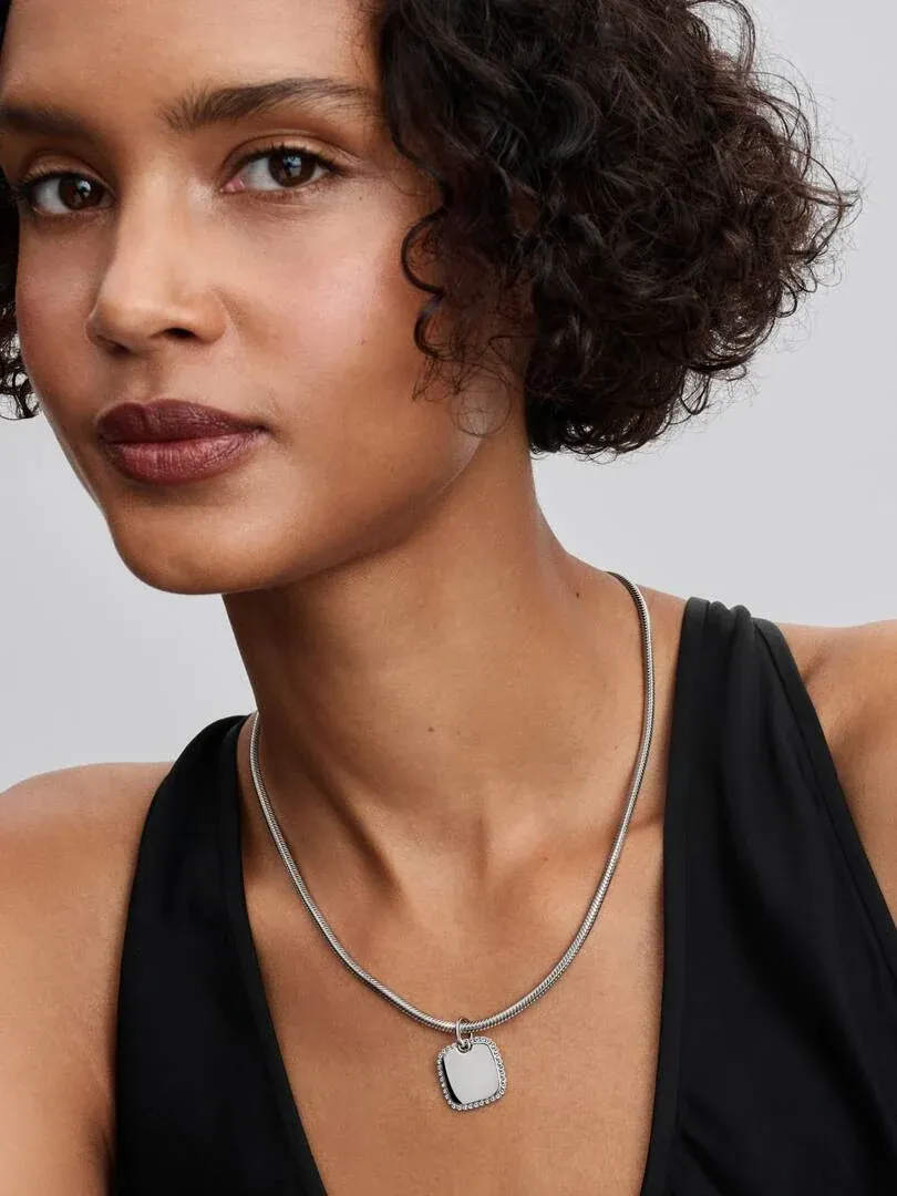 Nahaufnahme des quadratischen Anhängers mit Zirkonia-Besatz am Hals eines Models, neutraler Hintergrund.