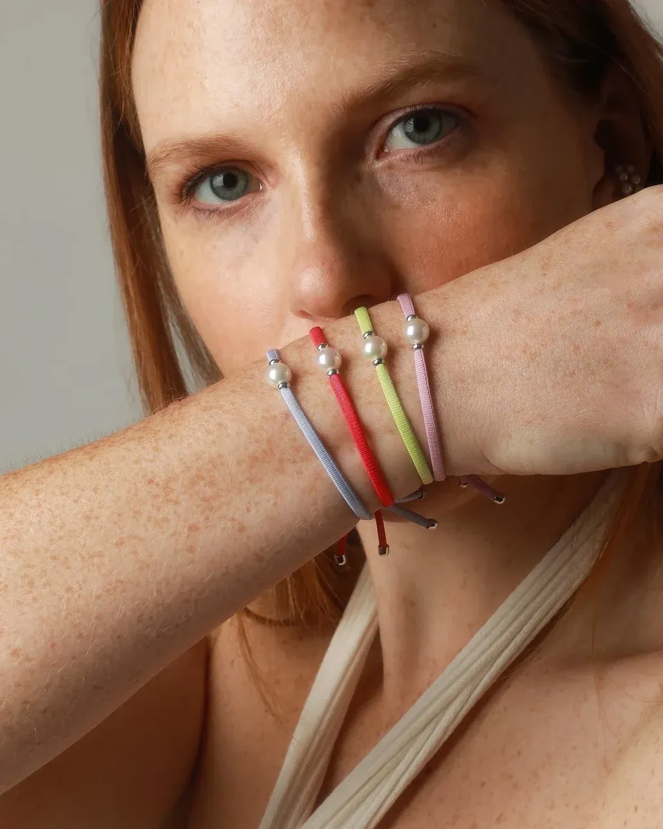 Primer plano de la muñeca con pulseras elásticas de colores y perlas, toma lateral sobre piel con pecas.