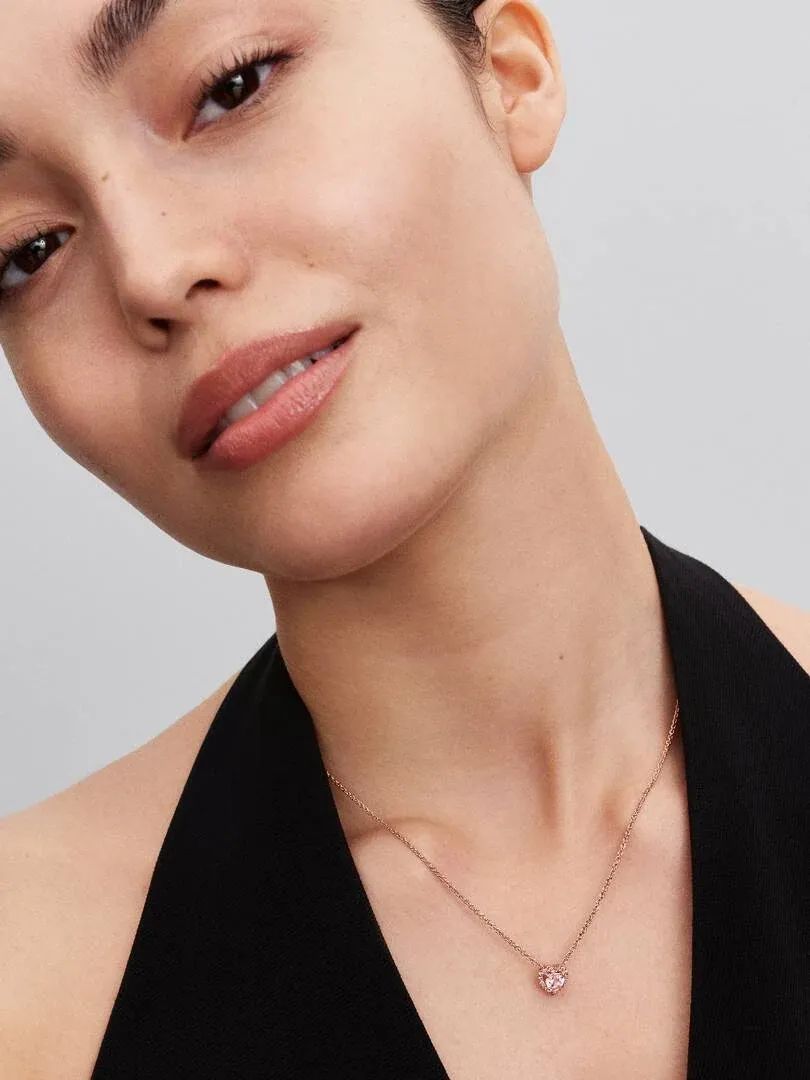 Primer plano del collar con colgante de corazón rosa sobre el cuello de una modelo, fondo neutro.