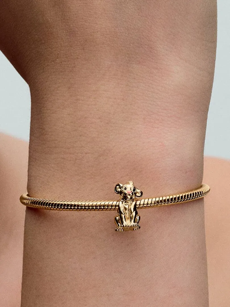 Close-up van de Simba charm aan een gouden armband, zijaanzicht om de pols gedragen.