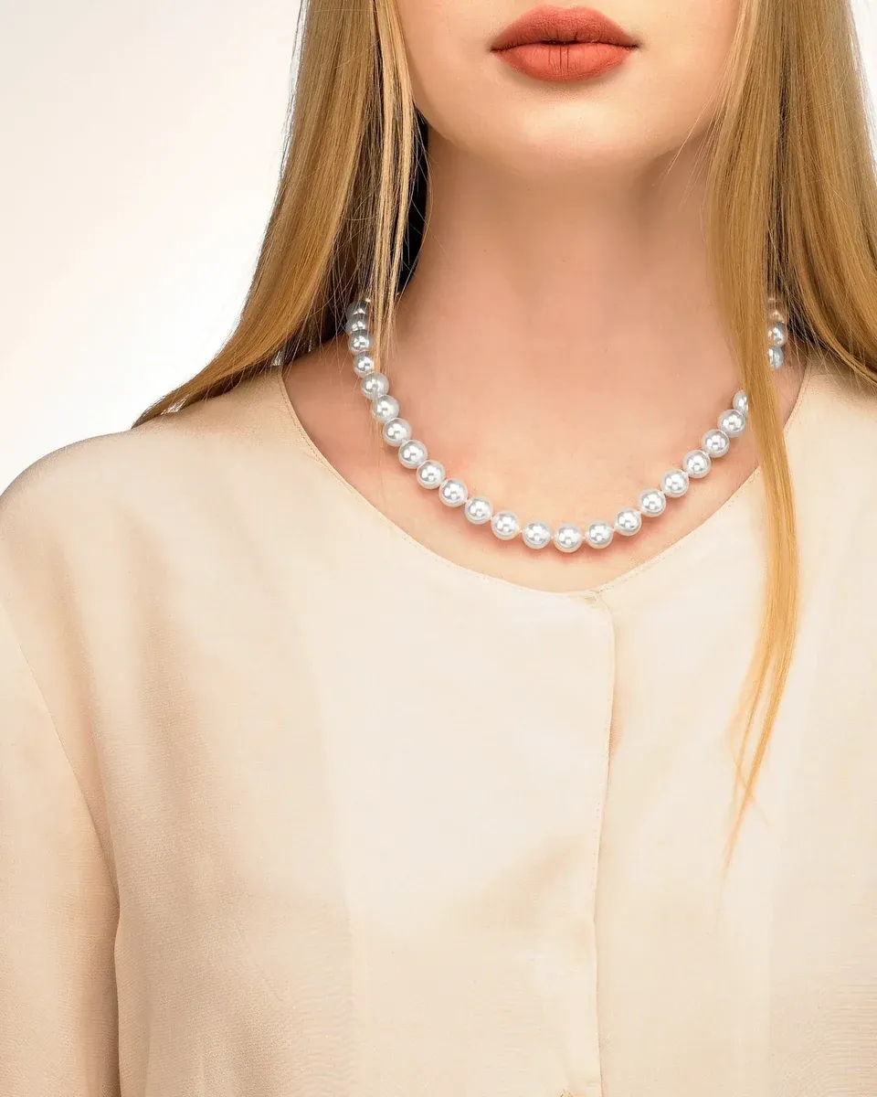 Gros plan du collier de perles sur le cou d'un mannequin, vue de face avec chemisier crème.