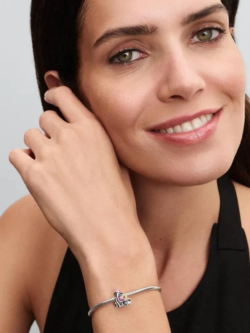 Close-up of the Dumbo charm on a silver bracelet worn on a wrist, soft blurred background.