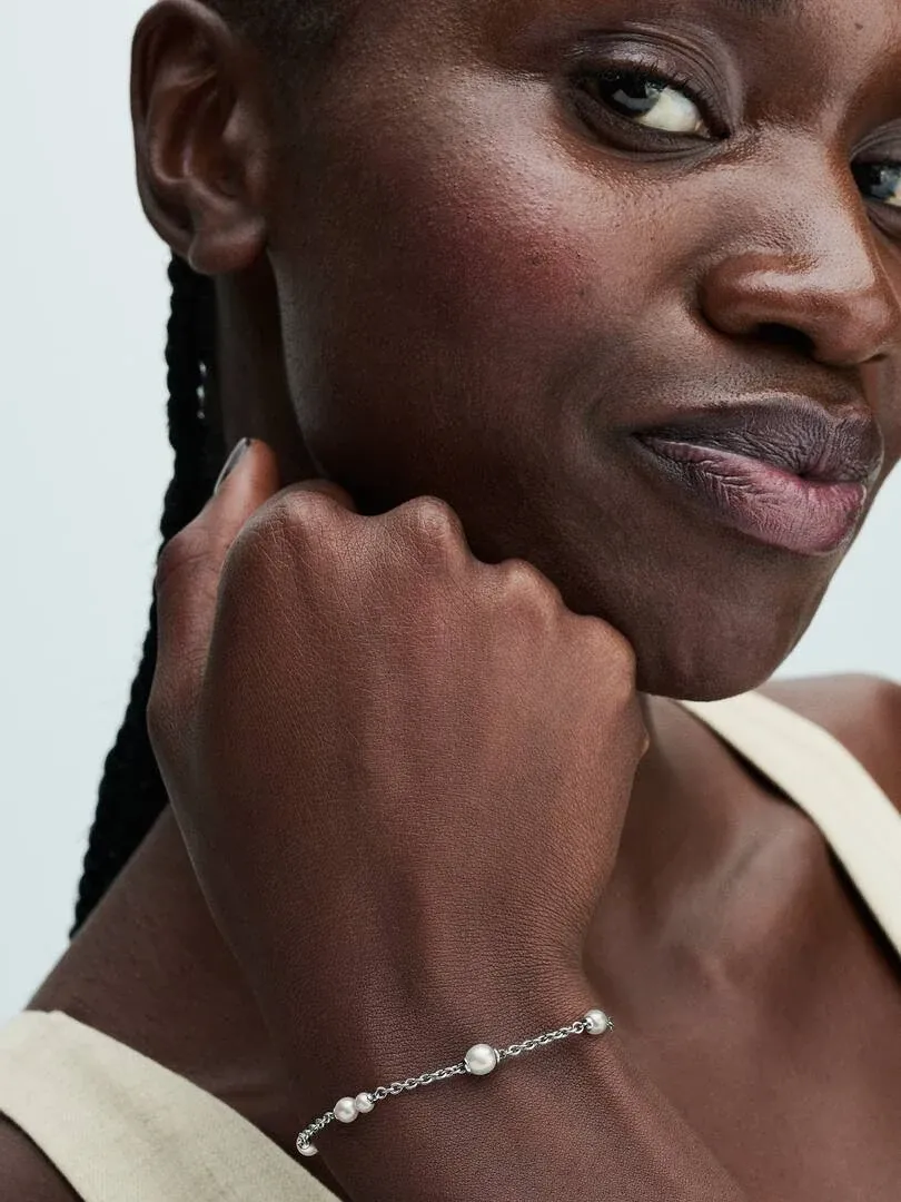 Nahaufnahme des Perlenarmbands am Handgelenk eines Models, Seitenansicht vor neutralem Hintergrund.