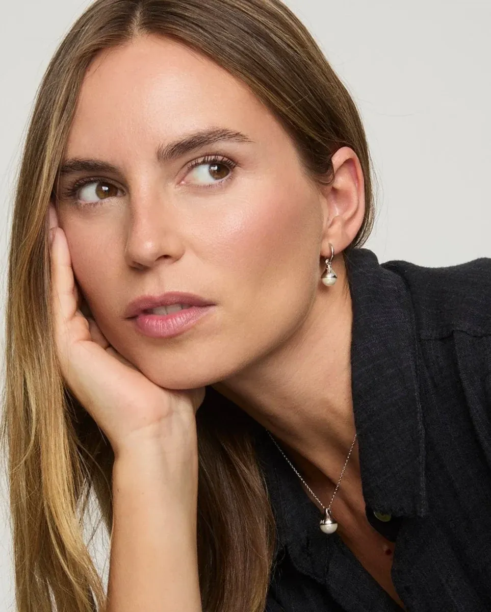 Close-up of model wearing pearl drop earrings and matching necklace, side view against neutral background.