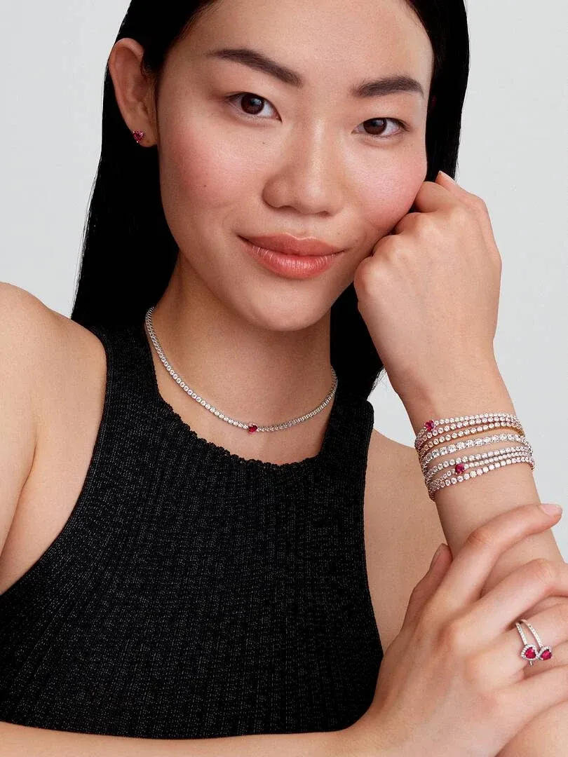 Model mit funkelnder Halskette, Tennisarmbändern und Herzring, Frontansicht vor neutralem Hintergrund.