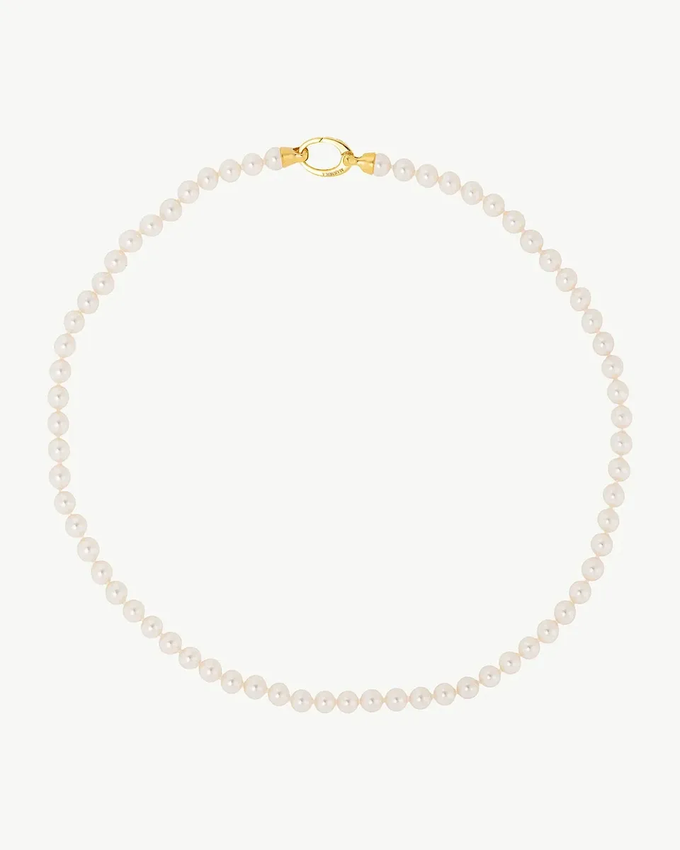 Collar de perlas dispuesto en círculo sobre fondo blanco, vista cenital con el cierre dorado en la parte superior.