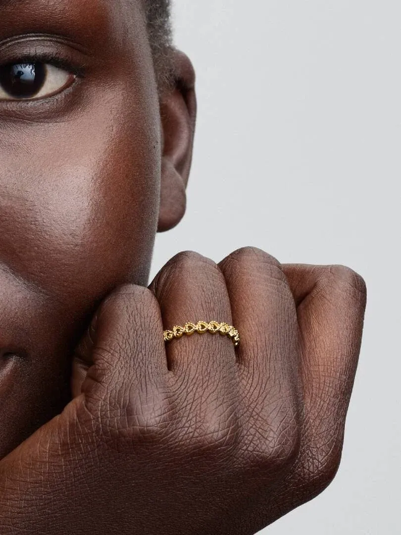 Nahaufnahme des goldenen Herz-Filigran-Rings am Finger, Seitenansicht vor neutralem Hintergrund.