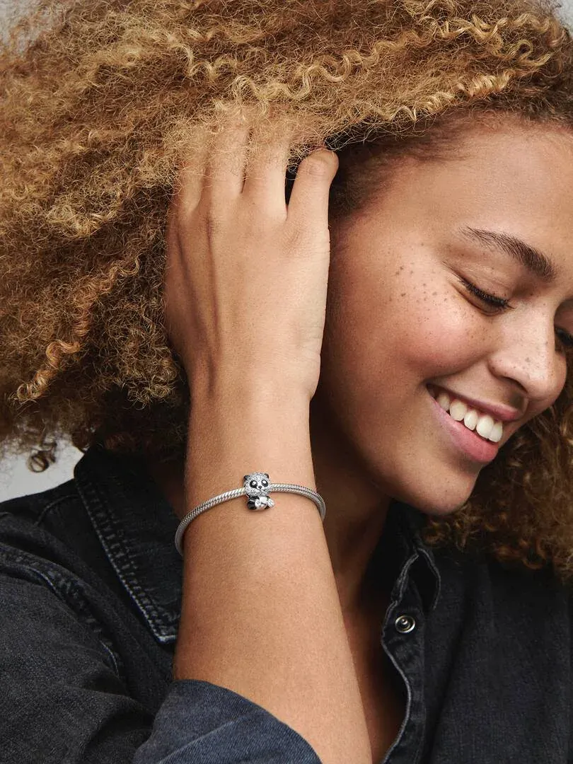 Nahaufnahme des Panda-Bären-Charms an einem Armband, getragen am Handgelenk eines Models vor unscharfem Hintergrund.