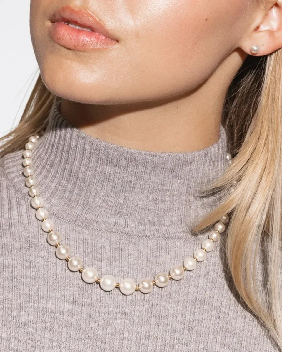 Primer plano del collar de perlas sobre cuello y jersey gris, toma frontal de la modelo.