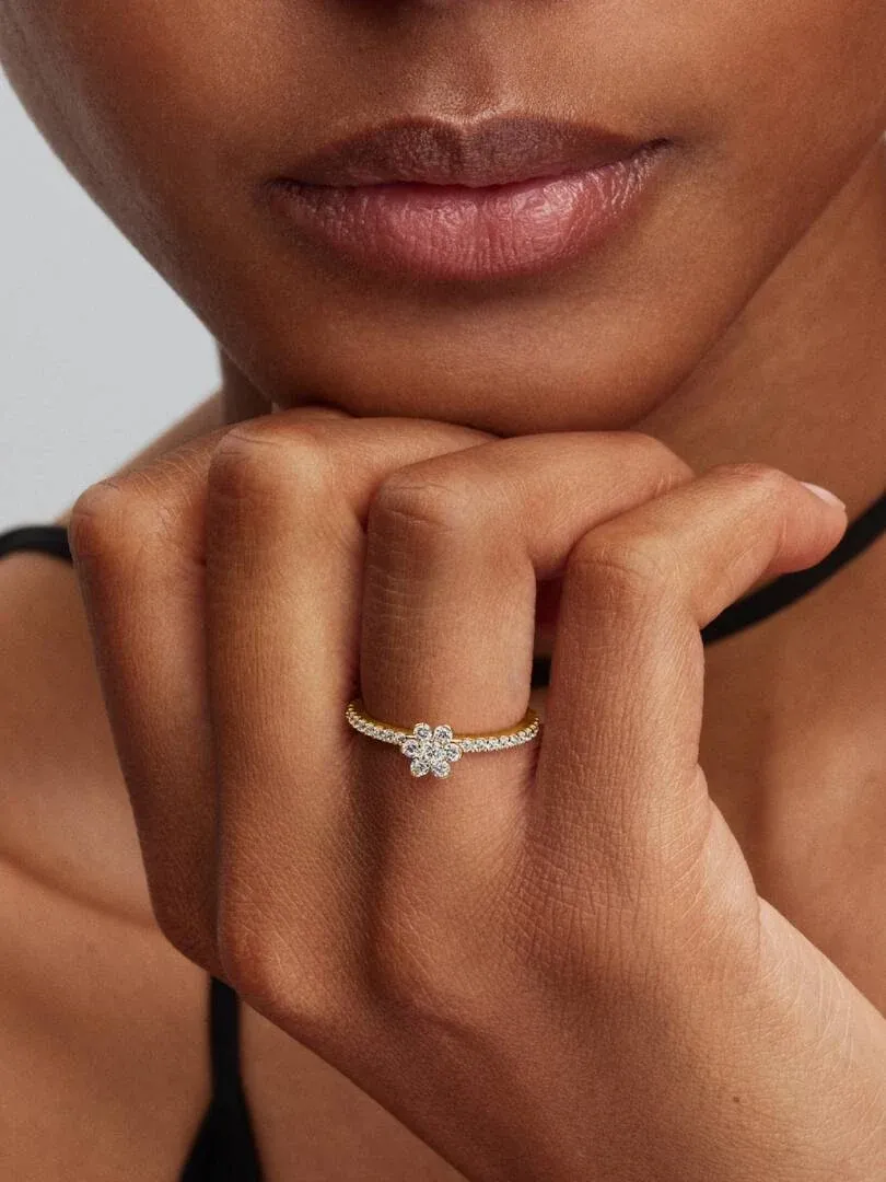 Close-up of the flower ring with cubic zirconia on a finger, side view against a blurred face background.