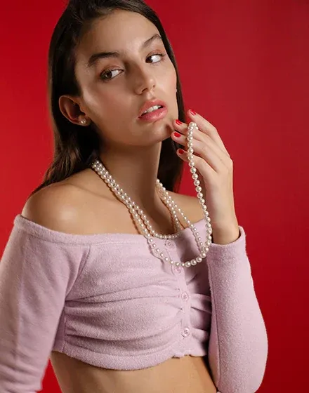 Primer plano de collar de perlas blancas sobre cuello y hombros, modelo con fondo rojo sólido.