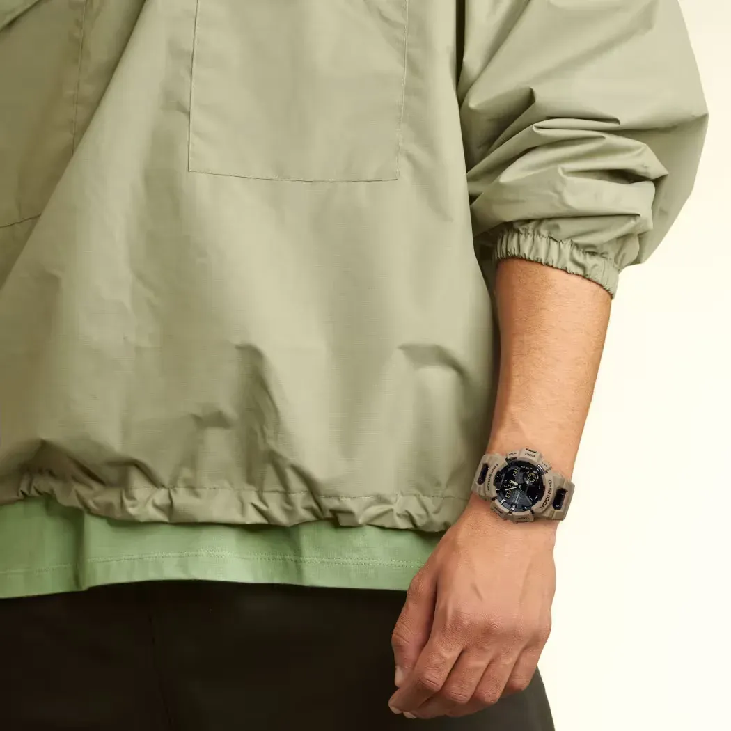 Reloj puesto en la muñeca de un modelo con chaqueta verde claro, fondo blanco neutro.