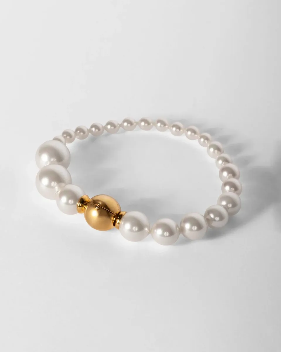 Pulsera de perlas blancas dispuesta en círculo sobre fondo blanco, vista desde un ángulo superior lateral.
