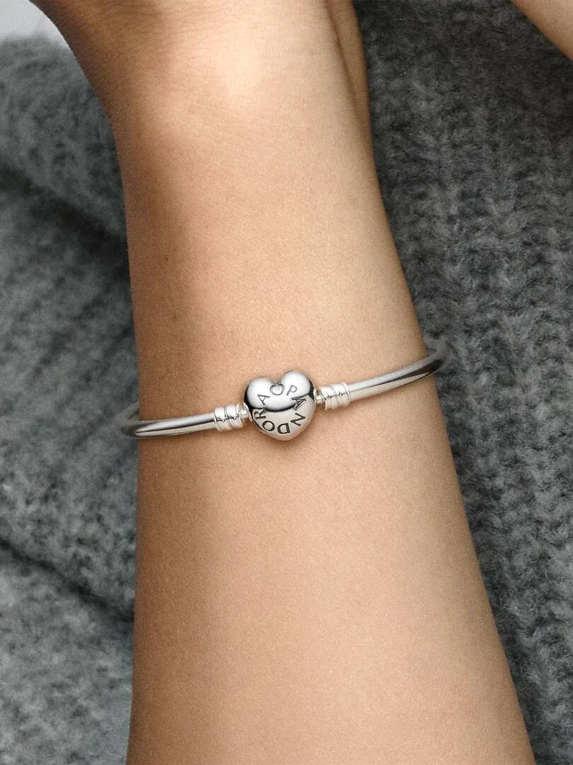 Close-up of the bangle with heart clasp on a wrist, blurred grey background.