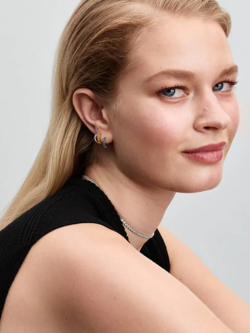 Nahaufnahme im Profil einer Model, die gelbe Kristall-Creolen und eine feine Halskette trägt.