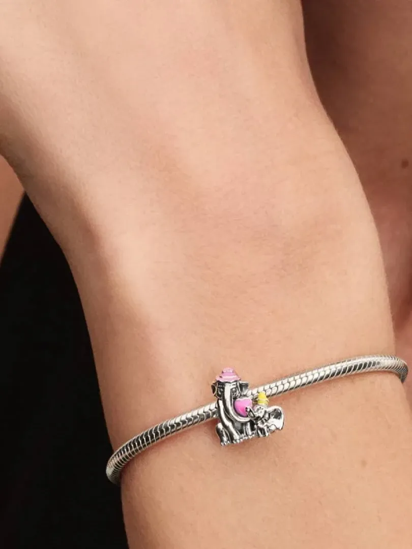 Close-up of the Dumbo charm on a silver bracelet, worn on a wrist with a blurred background.