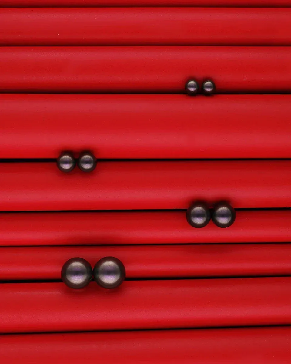 Trois paires de boucles d'oreilles en perles disposées sur une surface rouge texturée à rainures horizontales.