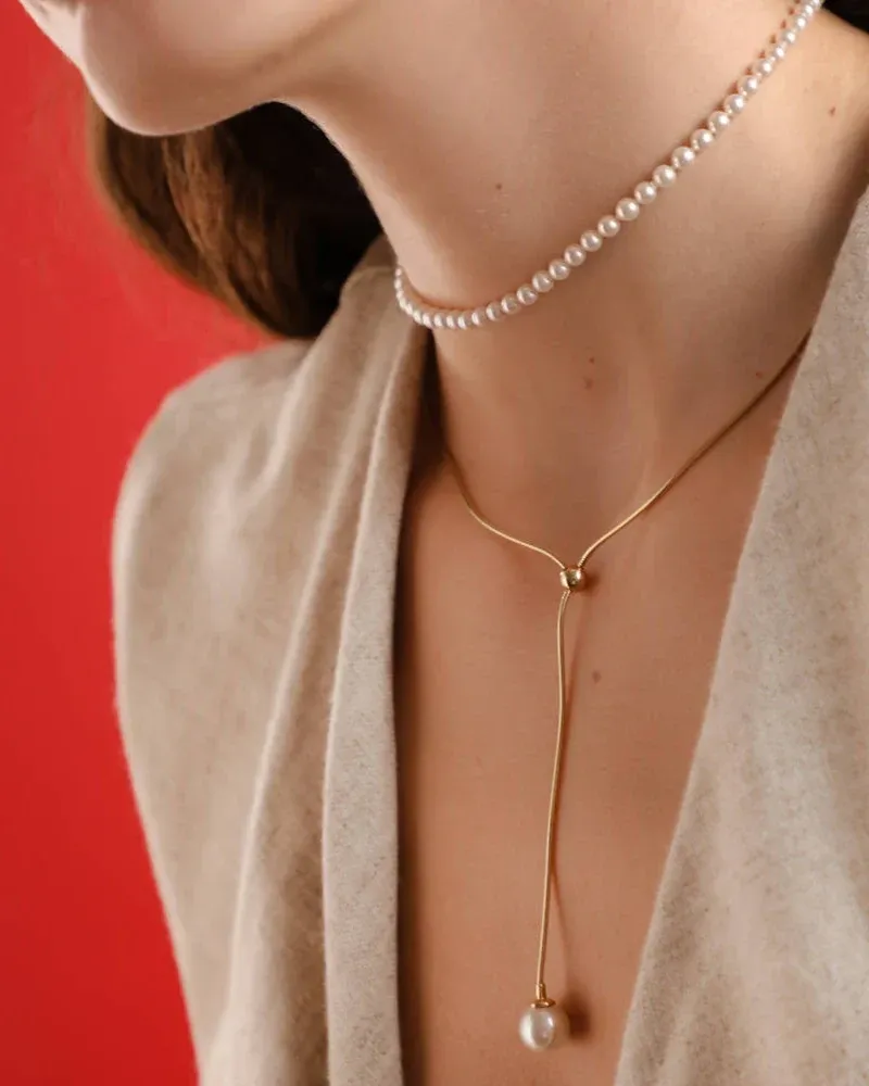 Gros plan latéral du collier avec perle sur le cou d'un modèle, fond rouge vif.