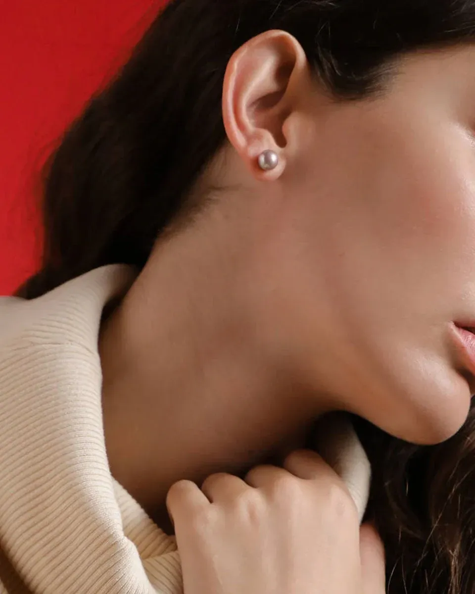 Side close-up of a pearl earring worn on the ear, vibrant red background.