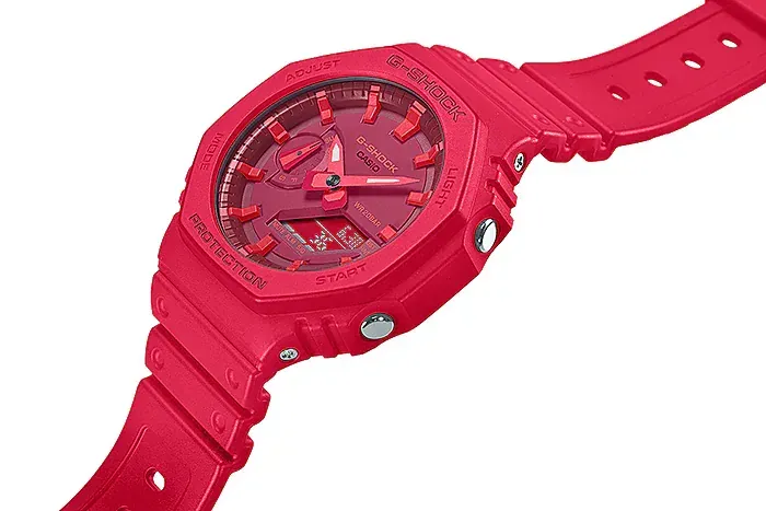 Primer plano en ángulo diagonal del dial y botones laterales del reloj rojo, fondo blanco.