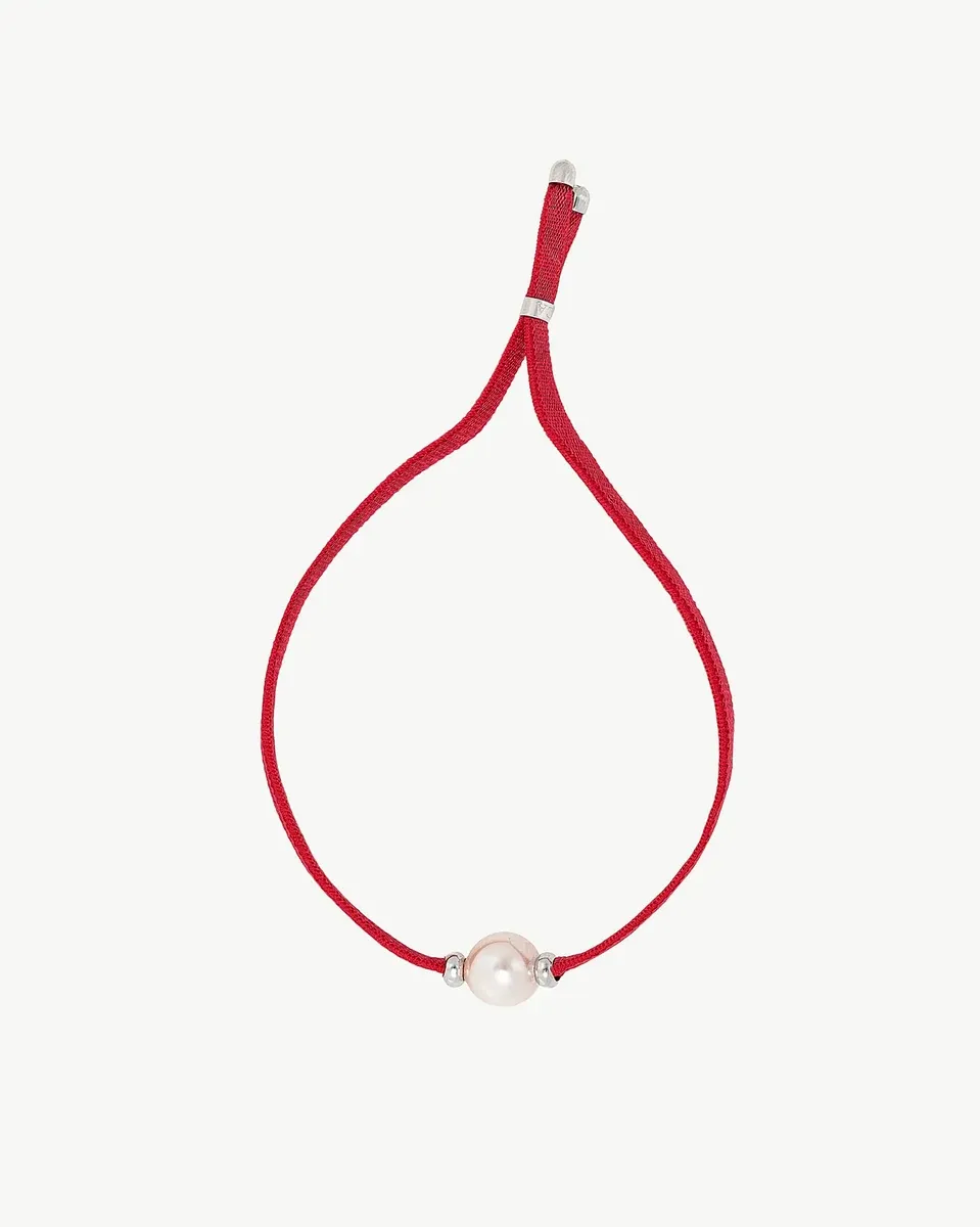 Vista frontal de la pulsera sobre fondo blanco, mostrando el cordón rojo coral y la perla blanca central.