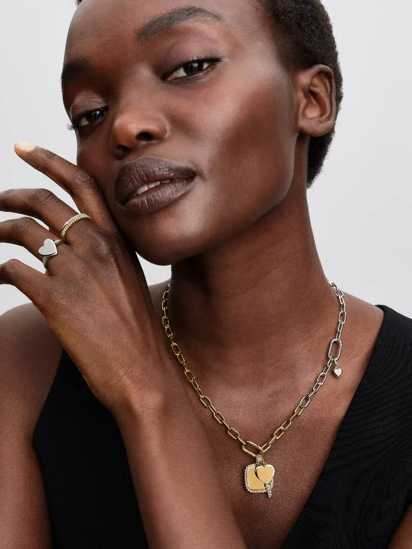 Close-up van een model met een schakelketting met hart hanger, vooraanzicht tegen een neutrale achtergrond.