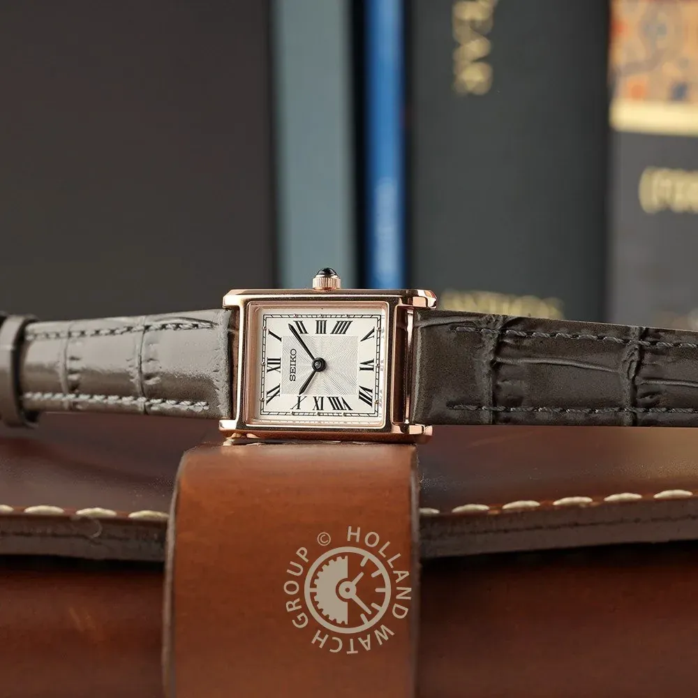 Reloj en plano frontal horizontal sobre superficie de cuero marrón con libros desenfocados al fondo