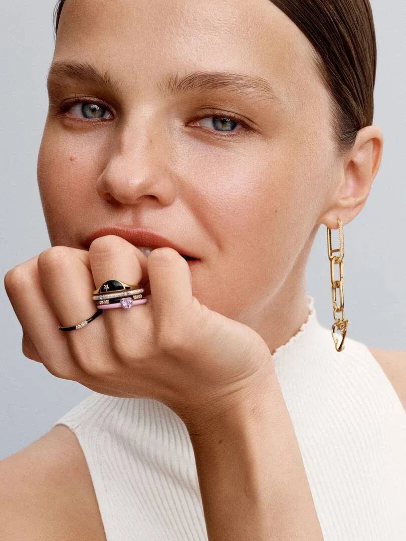 Nahaufnahme der Hand mit schwarzem Emaille- und Zirkonia-Ring, Model mit goldenem Kettenohrring.