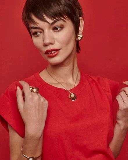 Close-up of model wearing pearl necklace and matching earrings against a vibrant red background.