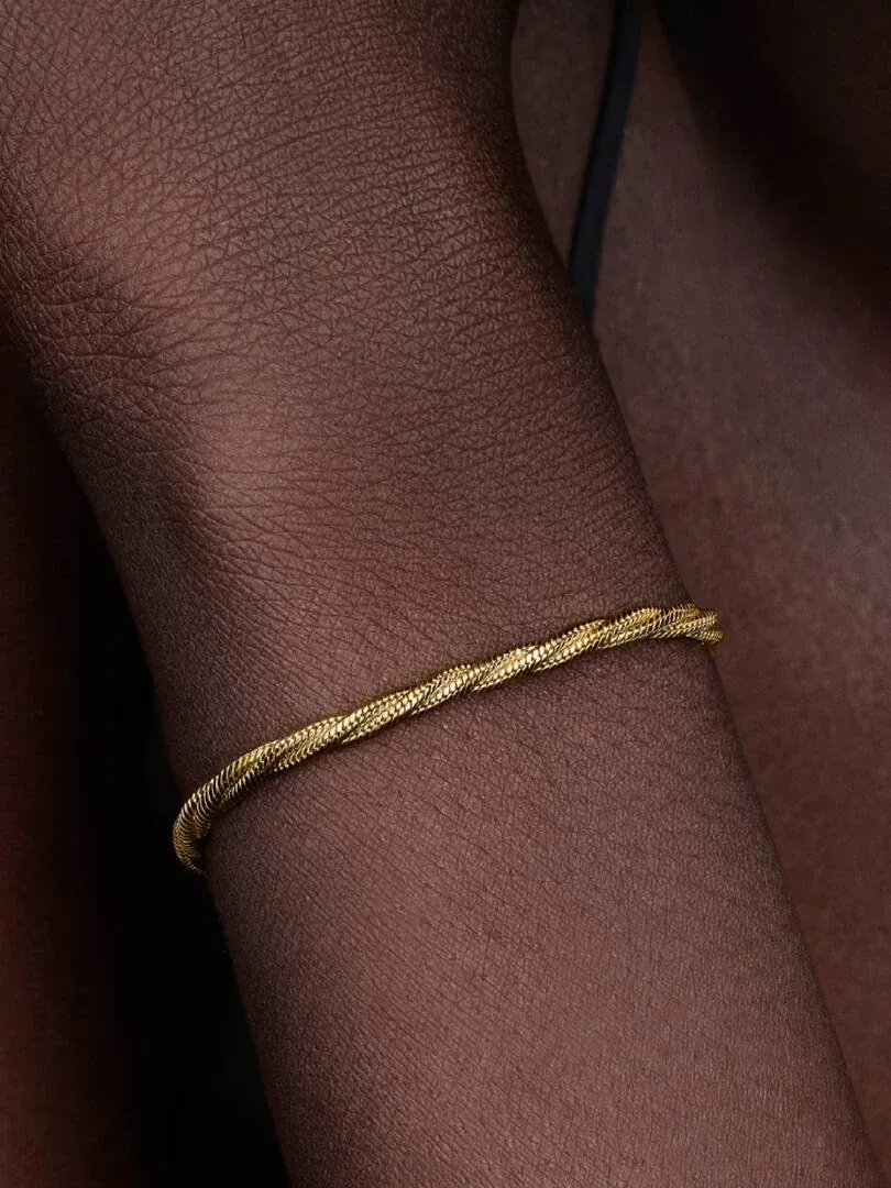Close-up of the gold braided bracelet worn on a wrist, side view with blurred background.