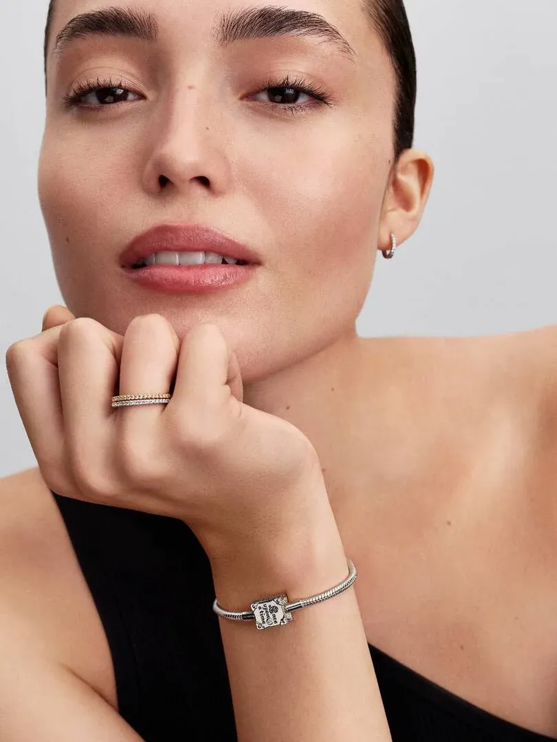 Close-up van een hand met een slangkettingarmband en ring, model tegen een neutrale achtergrond.