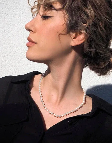 Zijaanzicht close-up van een vrouw met de parelketting over een zwart overhemd, witte achtergrond met natuurlijk licht.