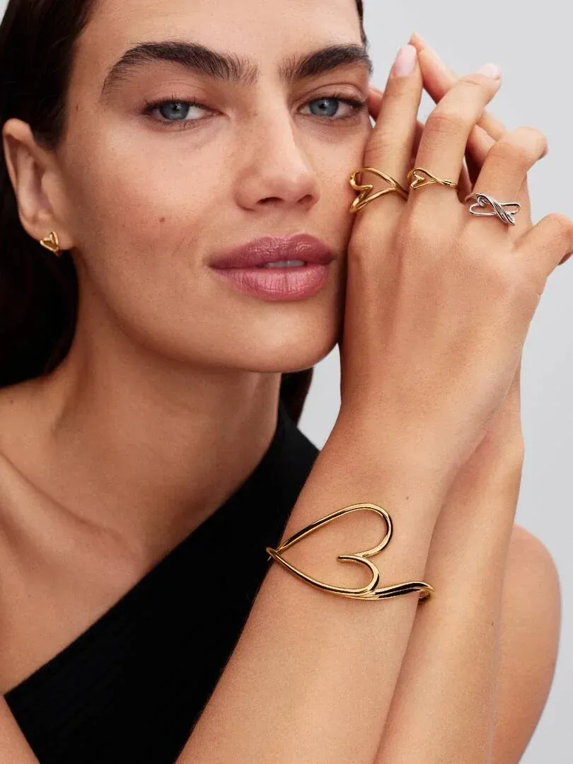 Close-up of hand wearing heart-shaped rings and bracelet on skin, blurred neutral background.