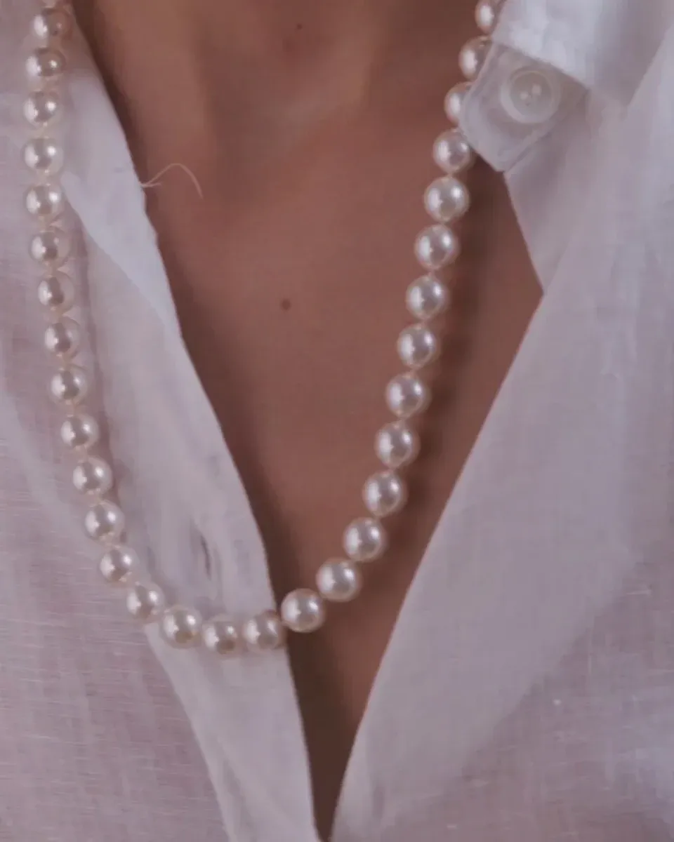 Gros plan du collier de perles sur le cou et une chemise blanche, vue de face mettant en valeur l'éclat des perles.