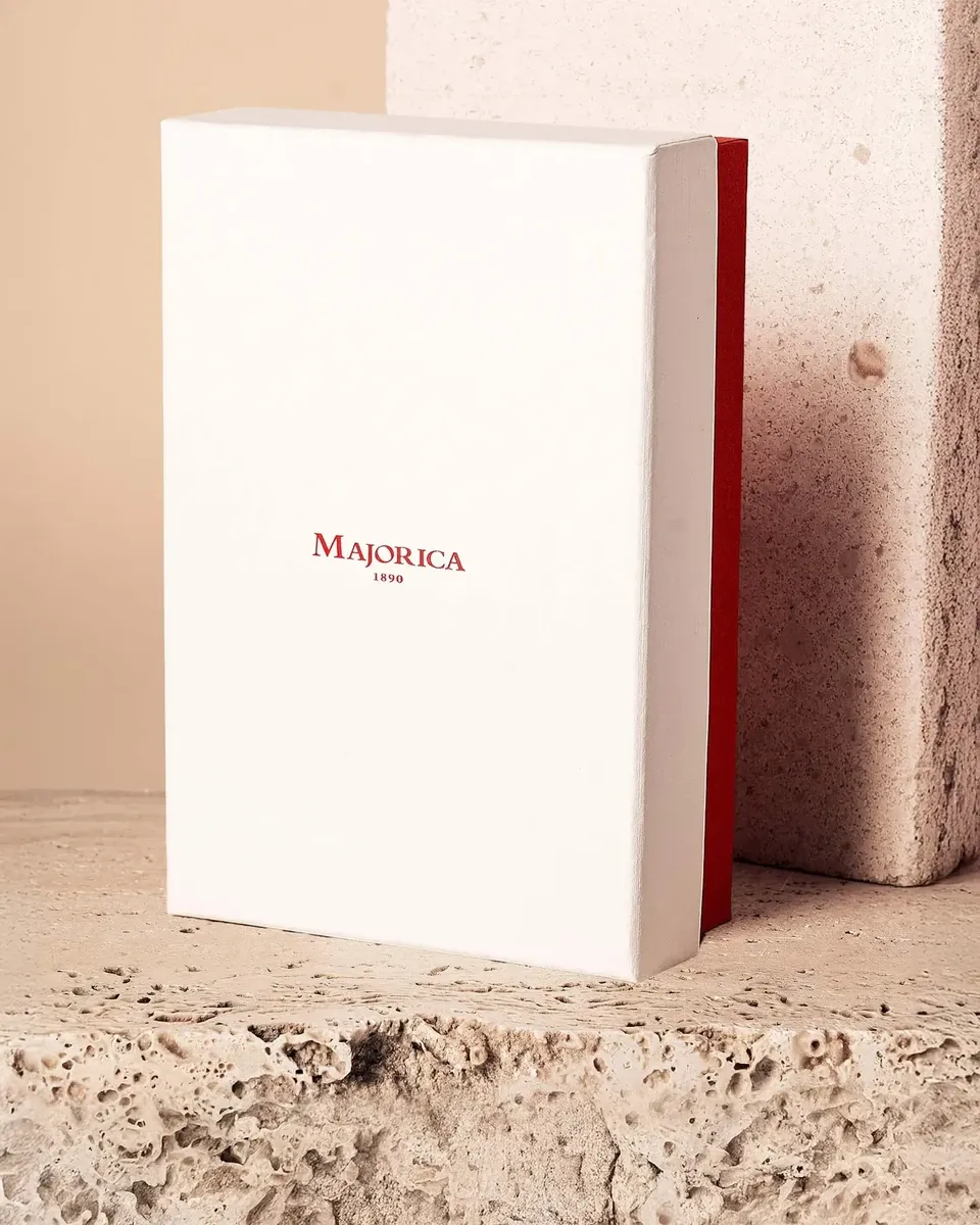 Witte etui met rood Majorica-logo op gestructureerd stenen oppervlak, zijvooraanzicht.