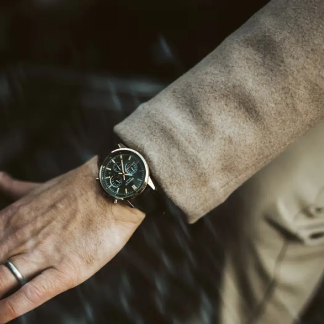Primer plano de reloj puesto en muñeca masculina con abrigo beige, fondo oscuro desenfocado.