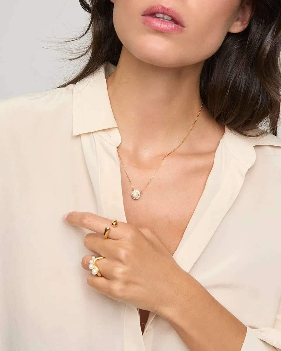Primer plano del collar con colgante de perla sobre el cuello y escote, modelo con blusa blanca.