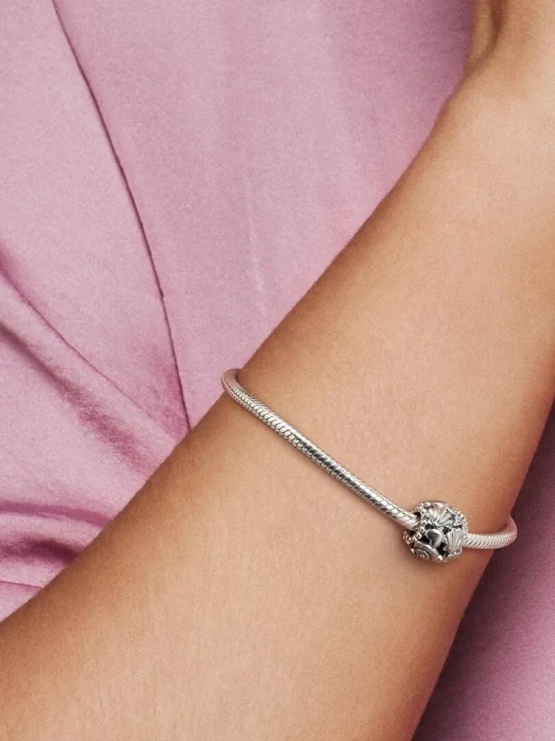 Close-up van de charm aan een zilveren armband om de pols, zijaanzicht met zachtroze achtergrond.