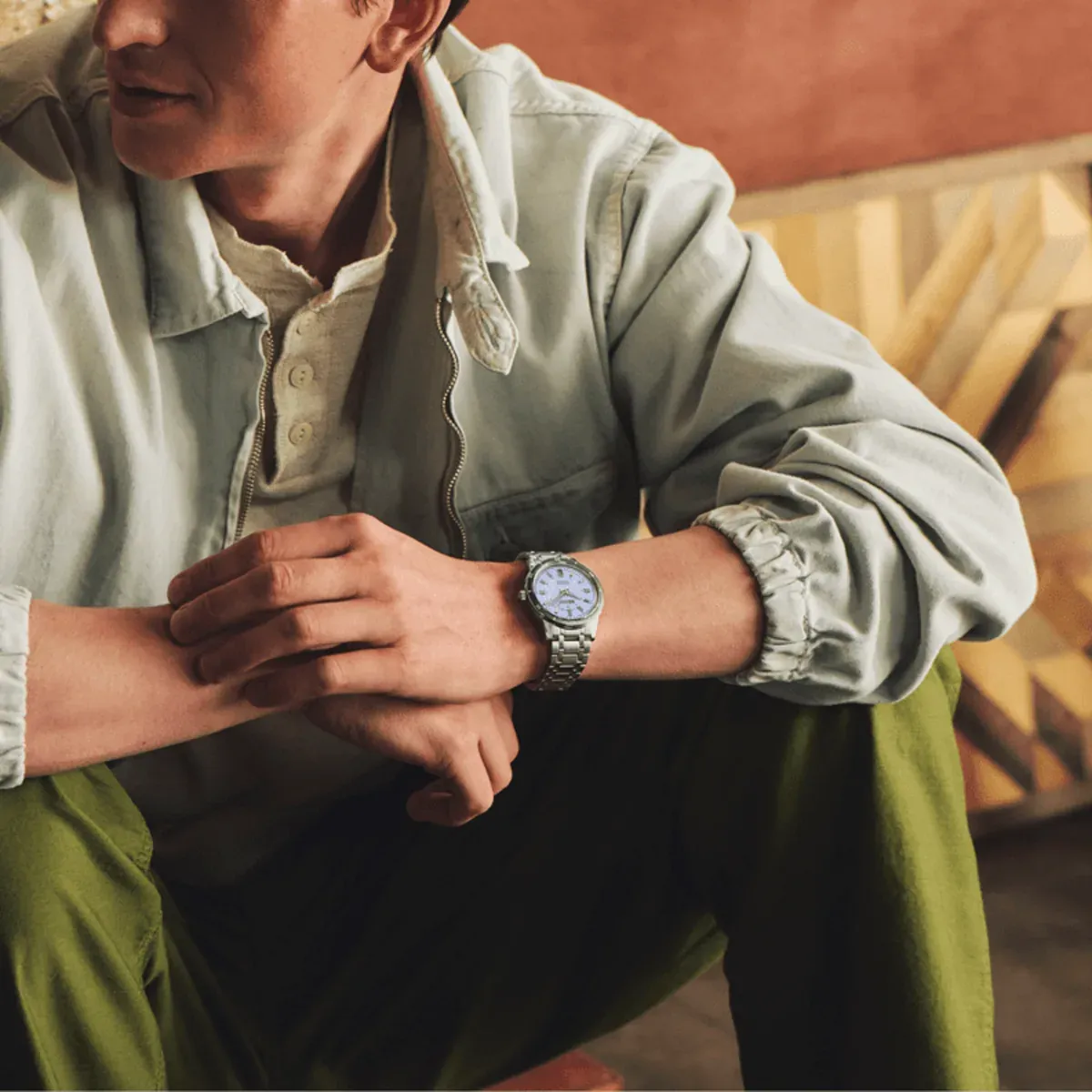 Medium shot of a man sitting with the watch on his wrist, blurred warm interior background.