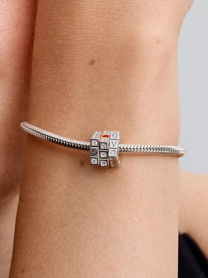Nahaufnahme des drehbaren Würfel-Charms an einem Silberarmband, getragen am Handgelenk eines Models.