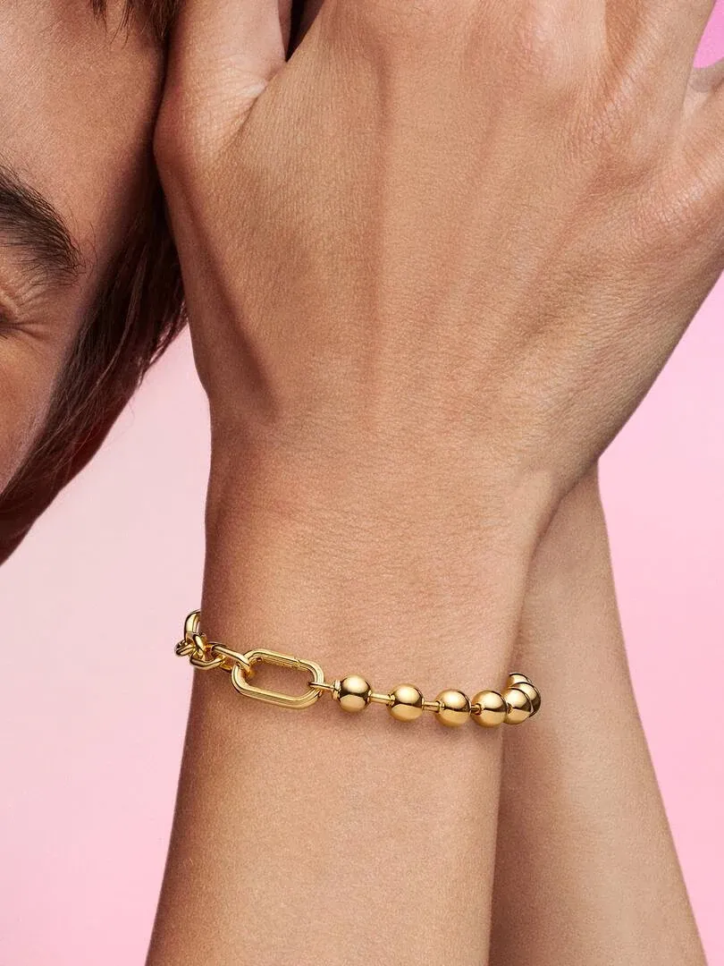 Nahaufnahme des goldenen Armbands am Handgelenk, Seitenansicht vor durchgehendem rosa Hintergrund.