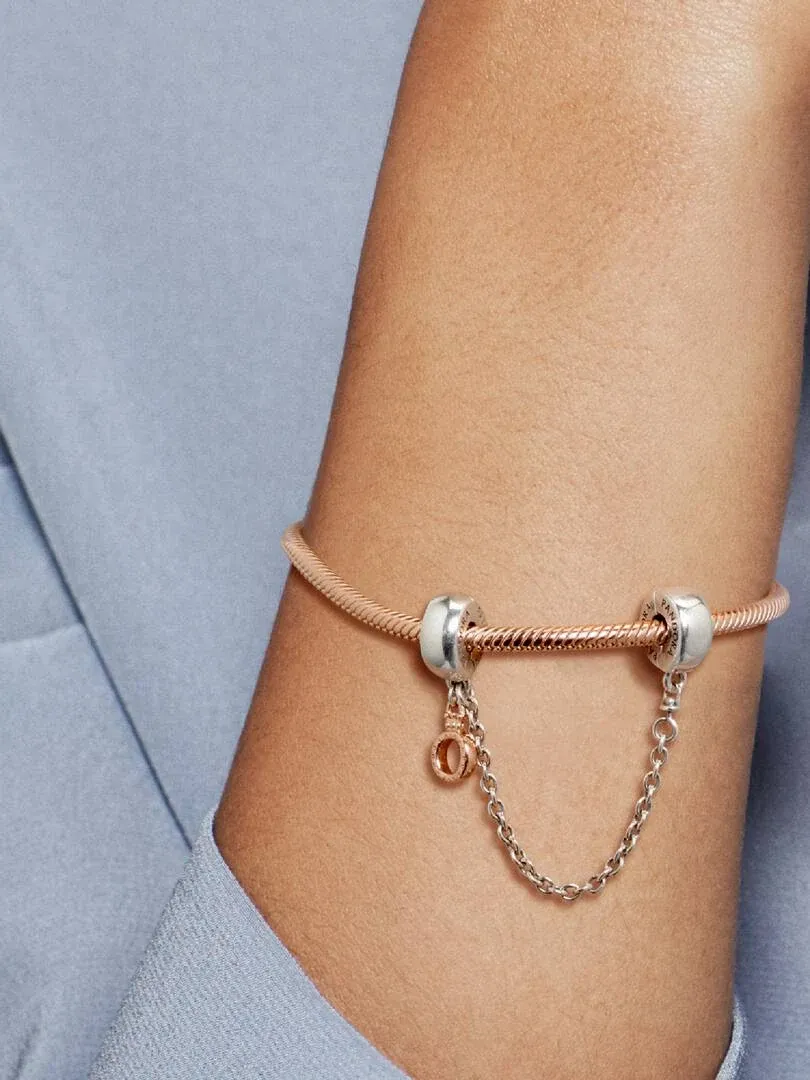 Close-up of the safety chain with crown charm on a wrist, soft blue blurred background.