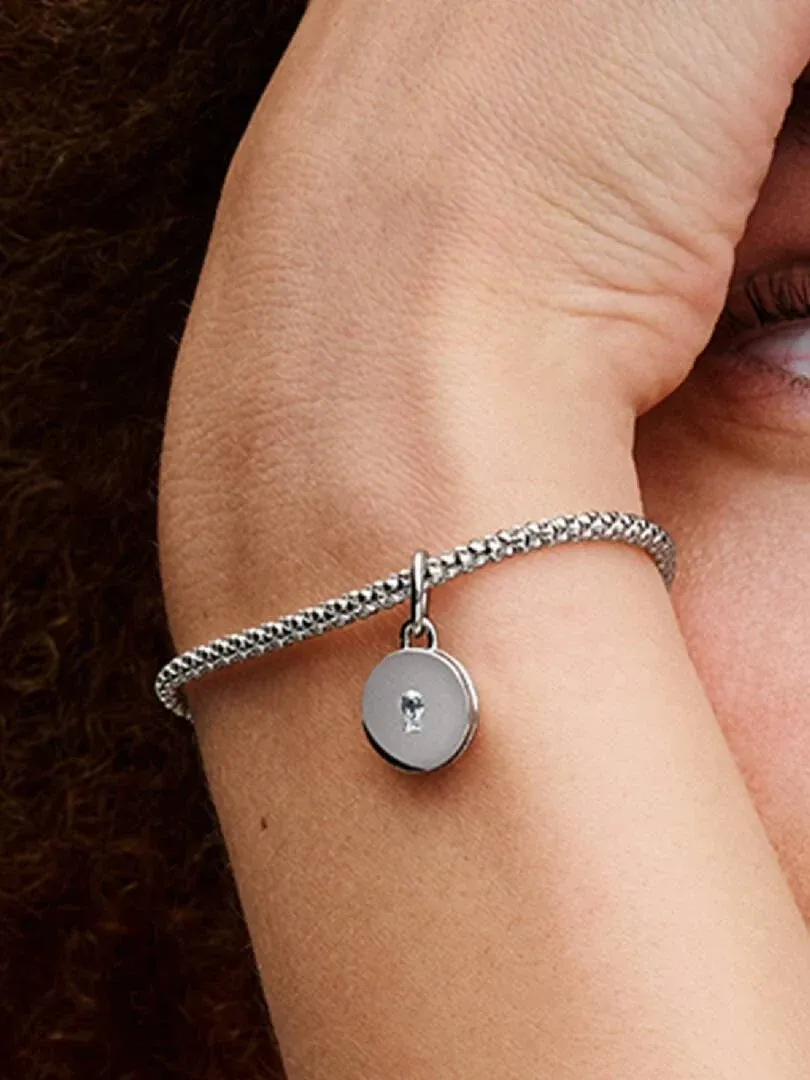 Nahaufnahme des Medaillon-Charms an einem Armband, getragen am Handgelenk vor weichem Hintergrund.