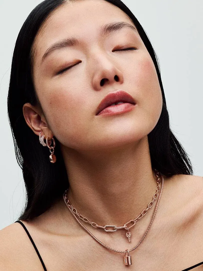Close-up of model wearing double rose gold chain necklace and matching earrings, neutral background.