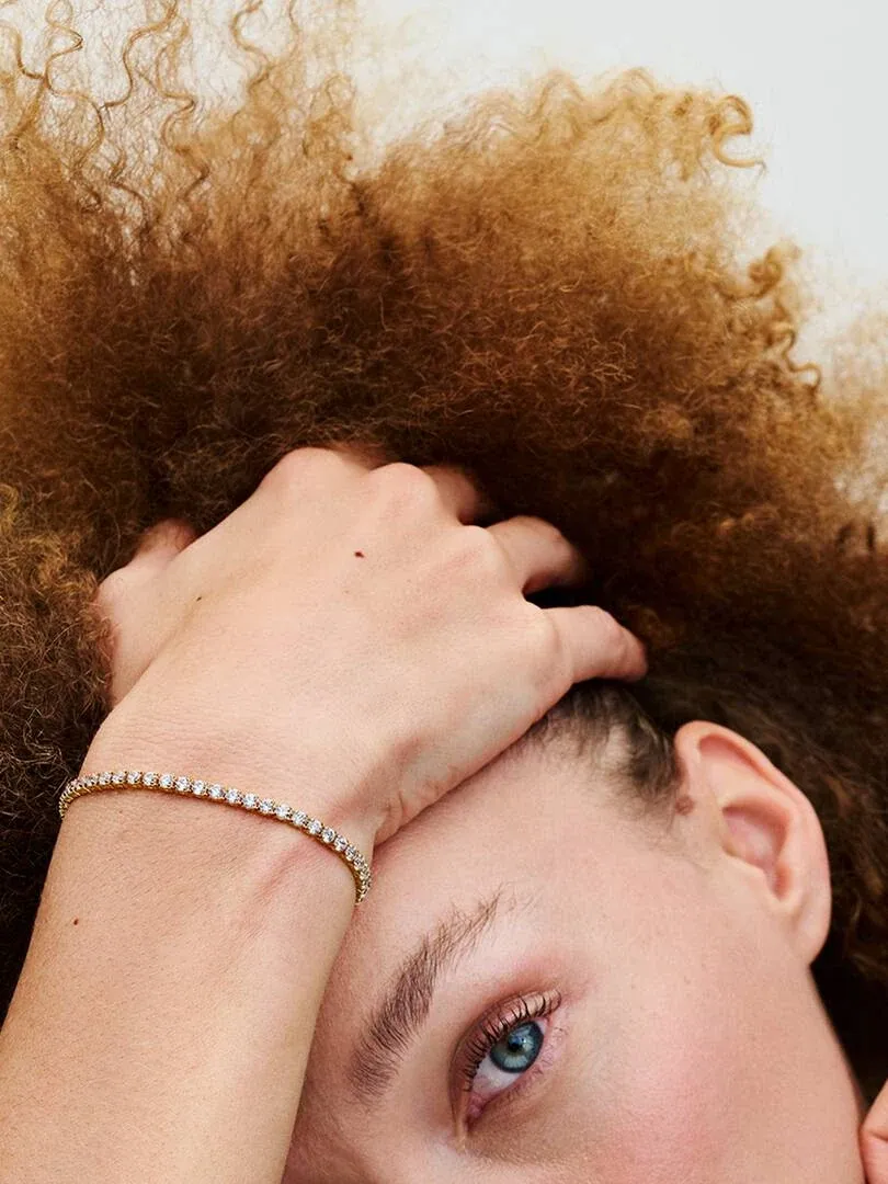 Nahaufnahme des goldenen Armbands am Handgelenk, Seitenansicht mit Modell und unscharfem lockigem Haar.