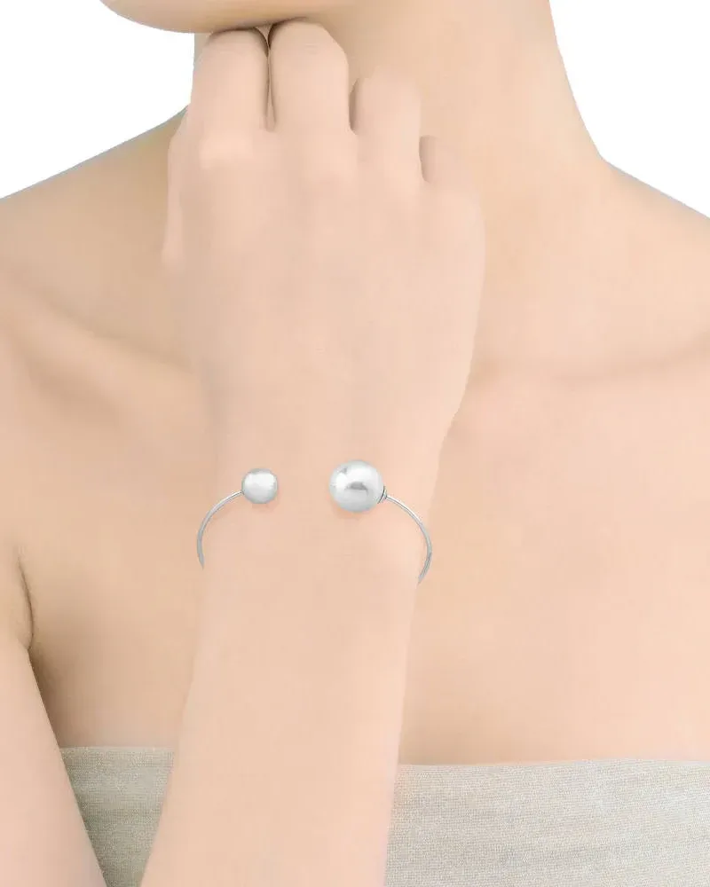 Stalen armband met witte parel om de pols gedragen, zijaanzicht op huid, neutrale achtergrond.