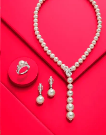 Conjunto de collar, pendientes y anillo sobre superficies geométricas rojas, toma cenital con sombras suaves.