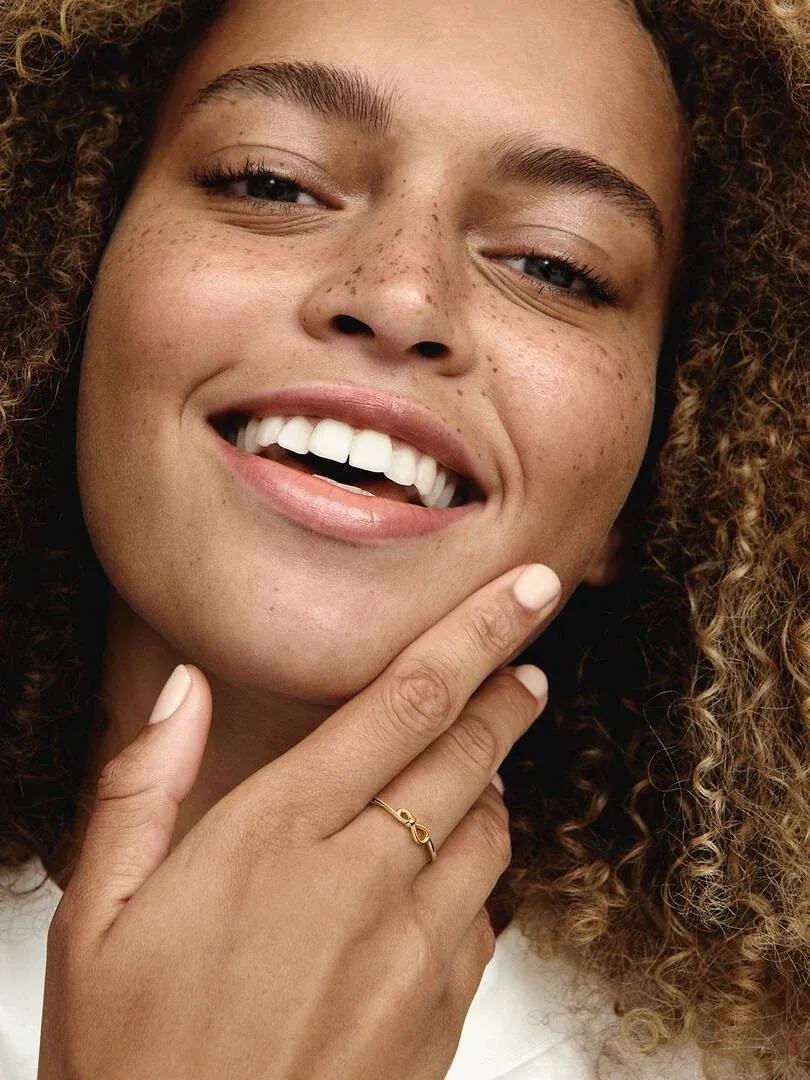 Close-up van een lachende vrouw met de gouden ring om haar vinger, zijaanzicht bij het gezicht.